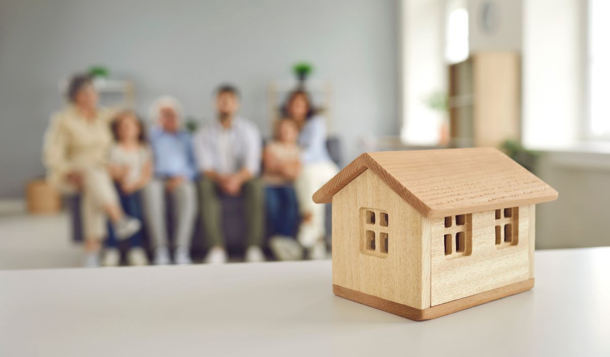 Closeup small little wooden toy house on table with blurred family on a background 